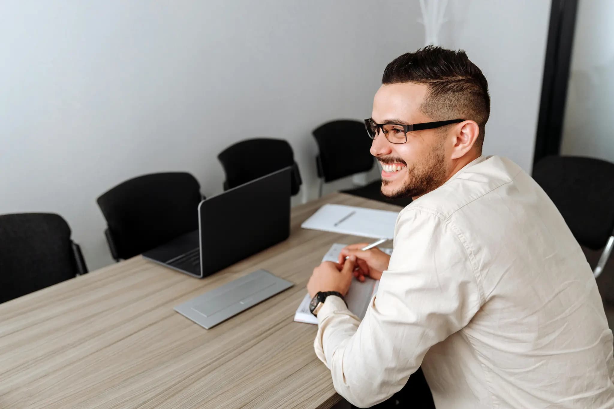 A person sitting at a conference table with a laptop, notepad, and pen, focusing on a discussion in a modern office environment.